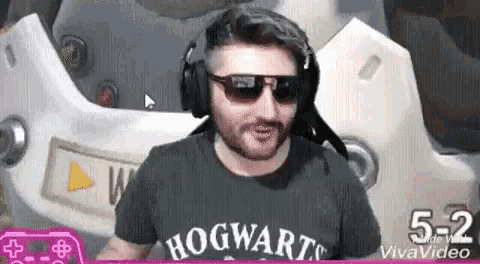 a man wearing headphones and sunglasses is playing a video game while wearing a hogwarts shirt .