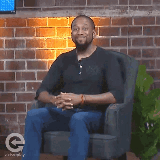 a man is sitting in a chair with a brick wall behind him and a logo for axisreplay