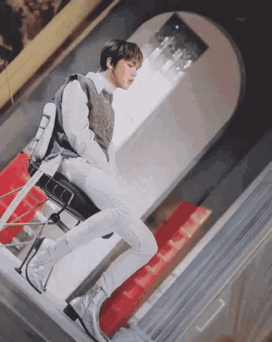 a young man is sitting on a chair with his legs crossed and a sweater that says ' nct ' on it