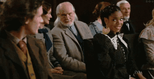 a group of people are sitting in a room and one of them is a woman in a black dress .