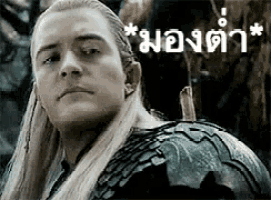 a man with long blonde hair is wearing a black armor and looking at the camera in a black and white photo .