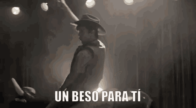 a man in a cowboy hat is standing on a stage with the words un beso para ti written below him