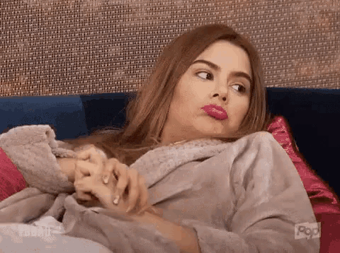 a woman in a robe is laying on a couch making a face .