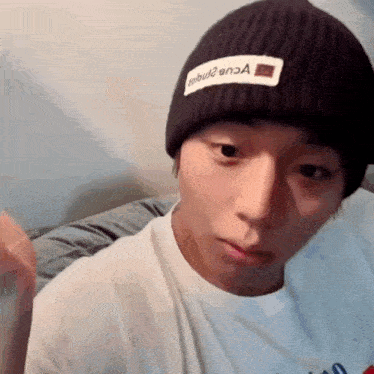 a man wearing a black beanie and a white t-shirt looks at the camera
