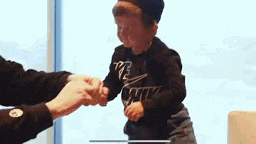 a little boy is shaking hands with a man in a black shirt .