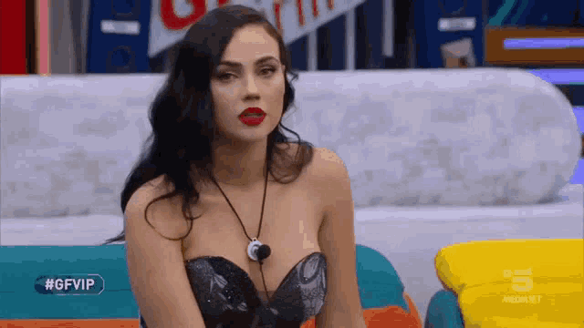 a woman is sitting on a couch wearing a black top and a necklace .