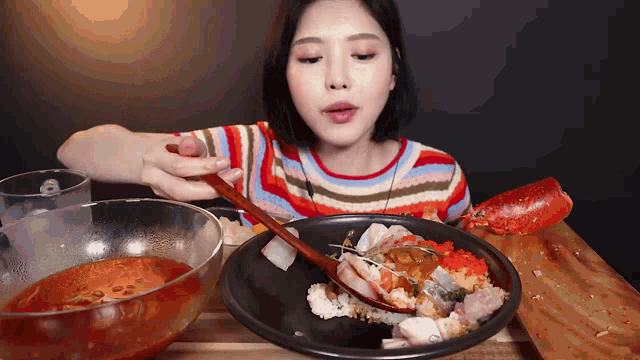 a woman in a striped shirt is eating a plate of food with a wooden spoon