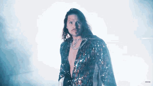 a man with long hair is wearing a sequined outfit and a necklace