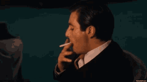 a man in a suit is smoking a cigarette while sitting in a chair .