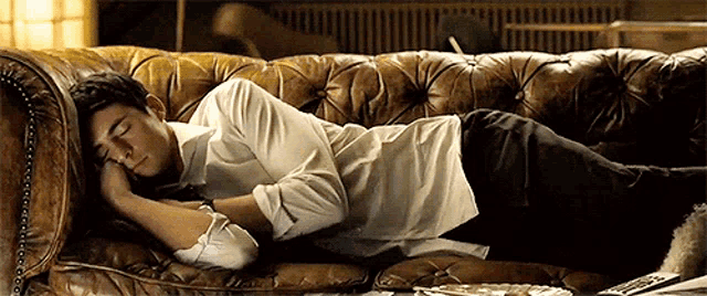 a man in a white shirt is sleeping on a leather couch