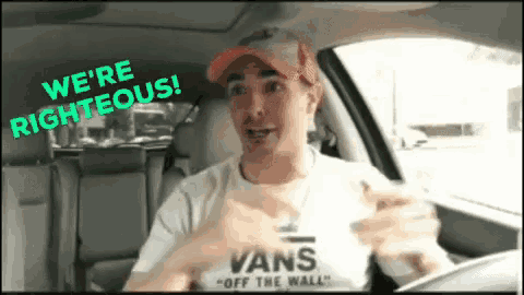 a man wearing a white vans off the wall shirt is driving a car