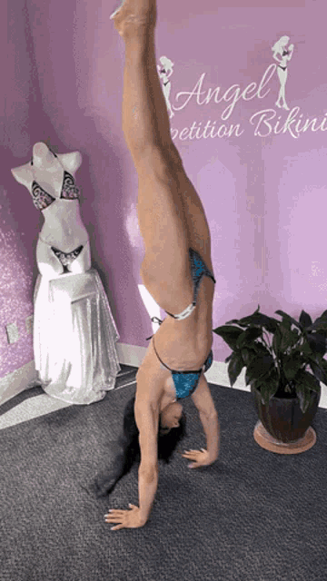 a woman is doing a handstand in front of a sign that says angel competition bikini