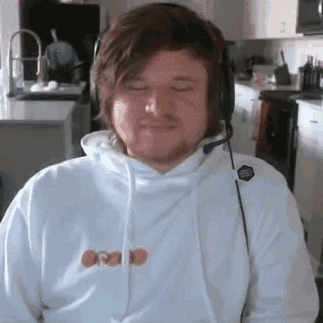 a man wearing a white hoodie and headphones is sitting in a kitchen .