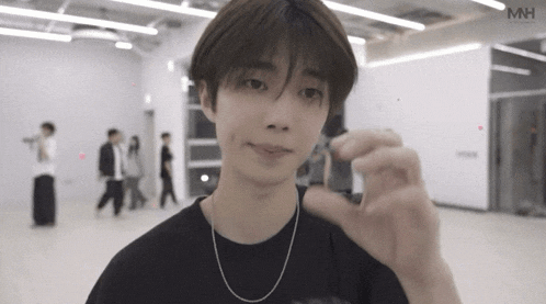 a young man wearing a black t-shirt and a chain around his neck is holding something in his hand .