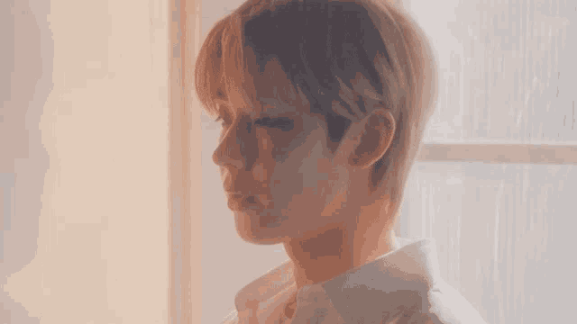 a young man in a white shirt is standing in front of a window looking out .