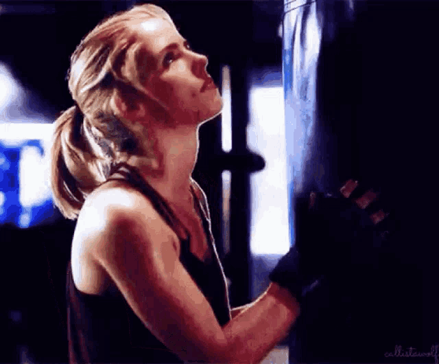 a woman is standing next to a punching bag in a gym looking up .