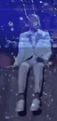 a man in a suit is sitting on a stage with his legs crossed in front of a microphone .