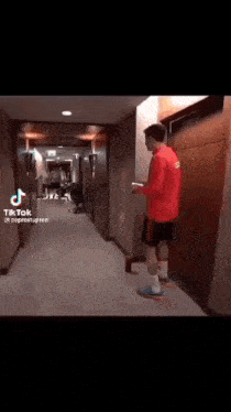 a man in a red shirt and shorts is standing in a hallway .