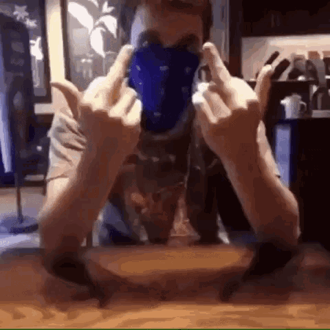 a man wearing a bandana on his face is giving the middle finger