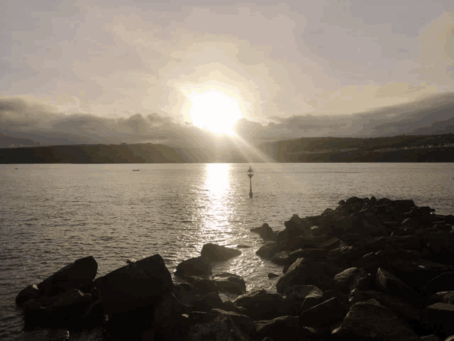 the sun shines brightly over a body of water with rocks in the foreground
