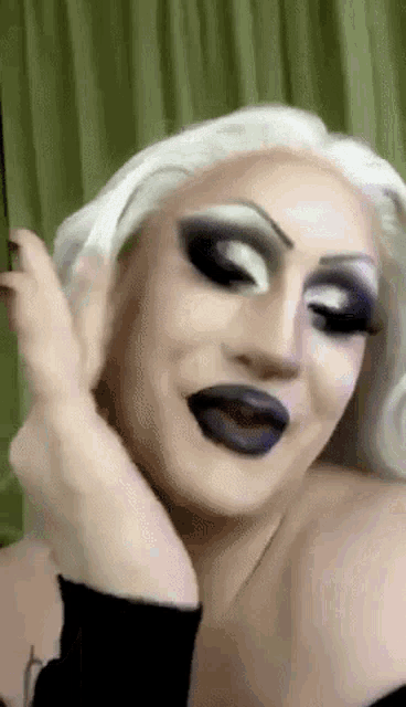 a drag queen is making a funny face with her hand on her face .