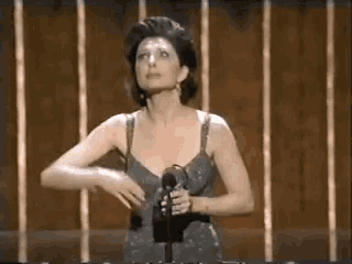 a woman in a dress is standing in front of a microphone and holding her breast .