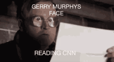 a man wearing glasses holds a piece of paper with the words gerry murphy 's face reading cnn