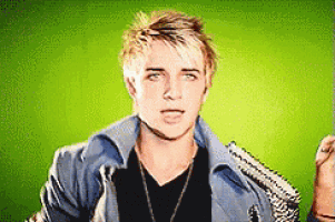 a man wearing a black shirt and a blue jacket is standing in front of a green background