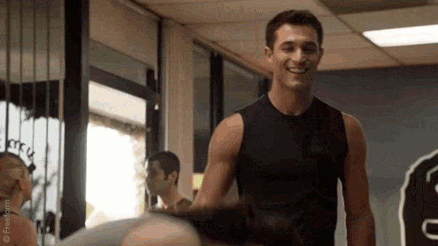 a man wearing a black tank top is smiling in a gym