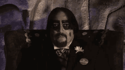 a man in a suit and tie is sitting on a couch in a dark room .