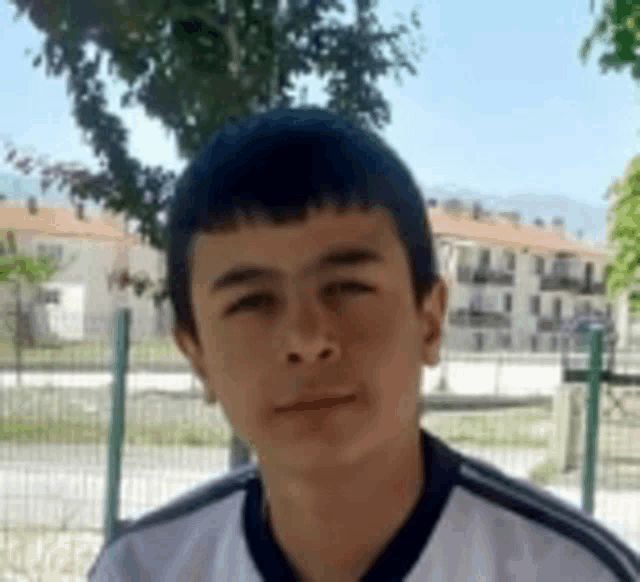 a young boy is sitting in front of a fence looking at the camera .