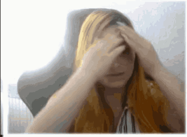 a woman with long red hair is covering her face with her hands while sitting in a chair .