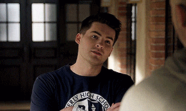 a man wearing a beverly high school t-shirt talks to another man