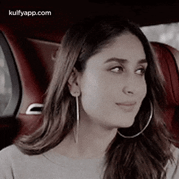 a woman wearing hoop earrings is sitting in a car and looking at the camera .
