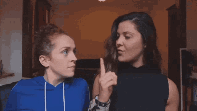 a woman in a blue hoodie points at another woman