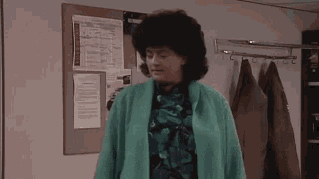 a woman in a green coat is standing in front of a bulletin board in a room .