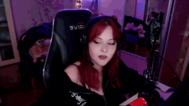 a woman with red hair is sitting in a gaming chair wearing headphones .
