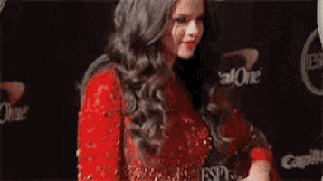 a woman in a red dress is standing on a red carpet and holding a microphone .