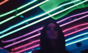 a woman is standing in front of a wall of neon lighting