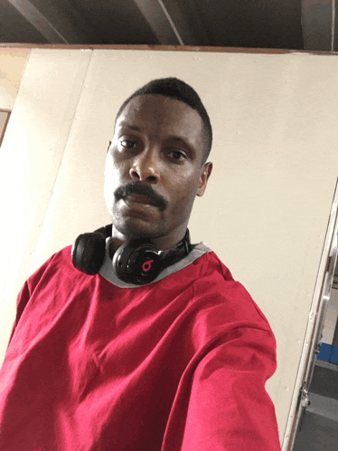 a man wearing a red shirt and headphones has the letter b on his neck