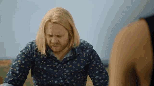 a man with long blonde hair and a beard is wearing a blue shirt with arrows on it