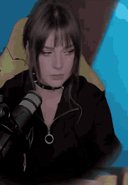 a woman wearing a choker is sitting in front of a microphone and looking at the camera
