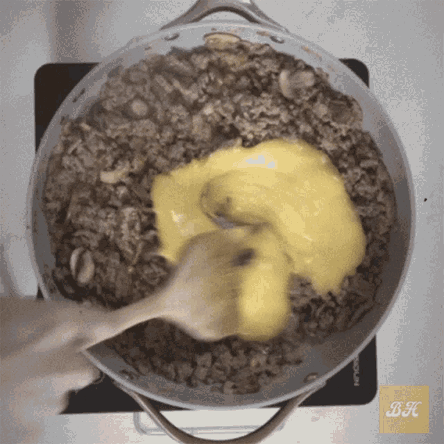 a person is stirring a pot of food with a wooden spoon and the letter bk is on the bottom left