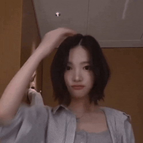 a woman with short hair is wearing a striped shirt and adjusting her hair .
