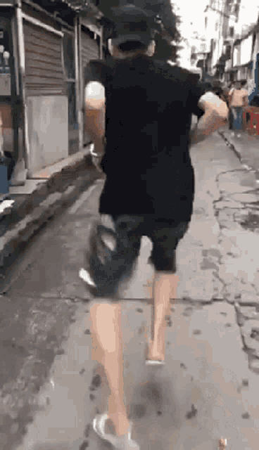 a man in a black shirt and shorts is running down a sidewalk .