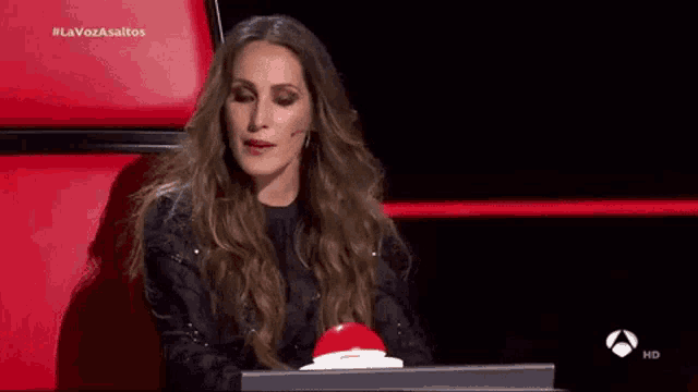 a woman is sitting in front of a red button and talking to someone .