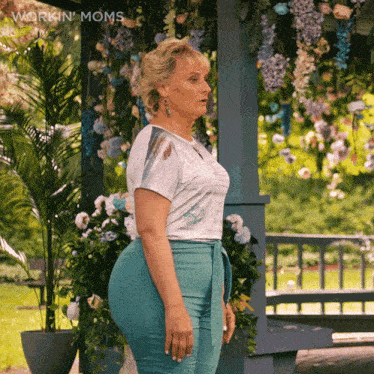 a woman in a white shirt and blue pants stands in front of a gazebo with flowers hanging from the ceiling