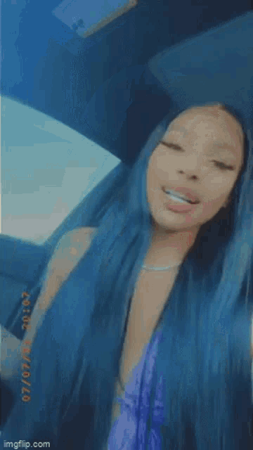 a woman with long blue hair is sticking her tongue out .
