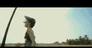 a woman with her hair blowing in the wind is standing in a field with trees in the background .