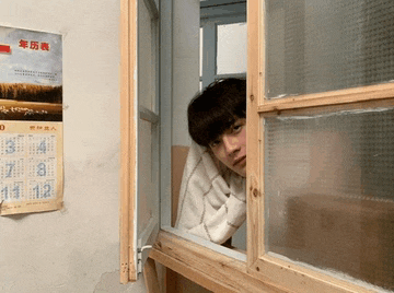 a person looking out a window with a calendar on the wall